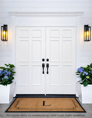 White double entry doors featuring the six piece door moulding kit, showcasing a classic paneled design framed by white trim and a door pediment with exterior wall lighting and blue hydrangeas.